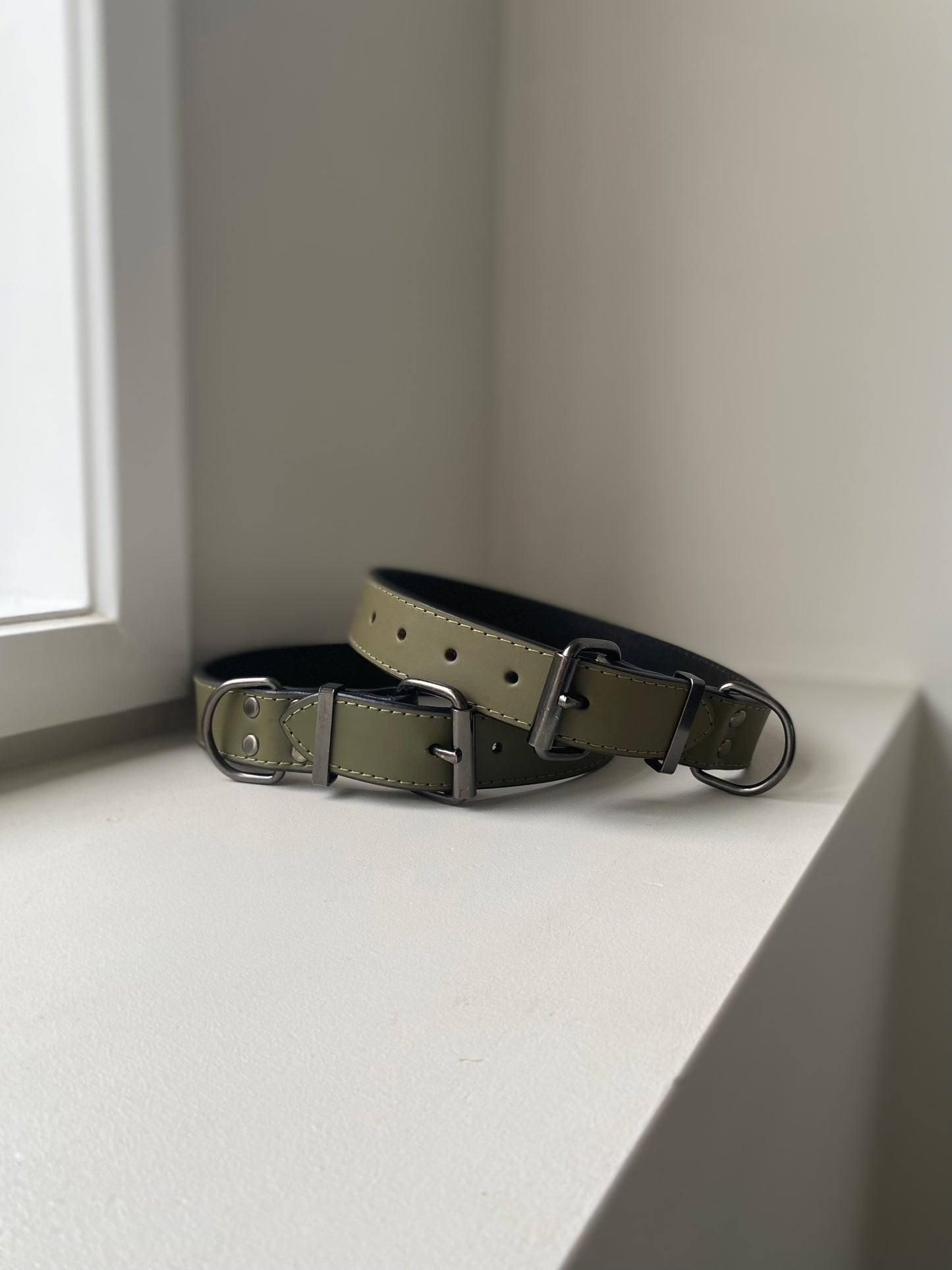 Two khaki green leather dog collars on a white surface with a neutral background