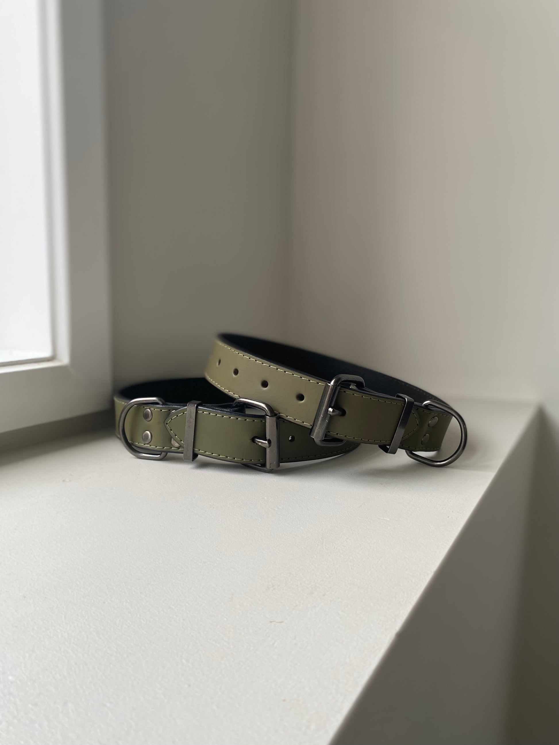 Two khaki green leather dog collars on a white surface with a neutral background