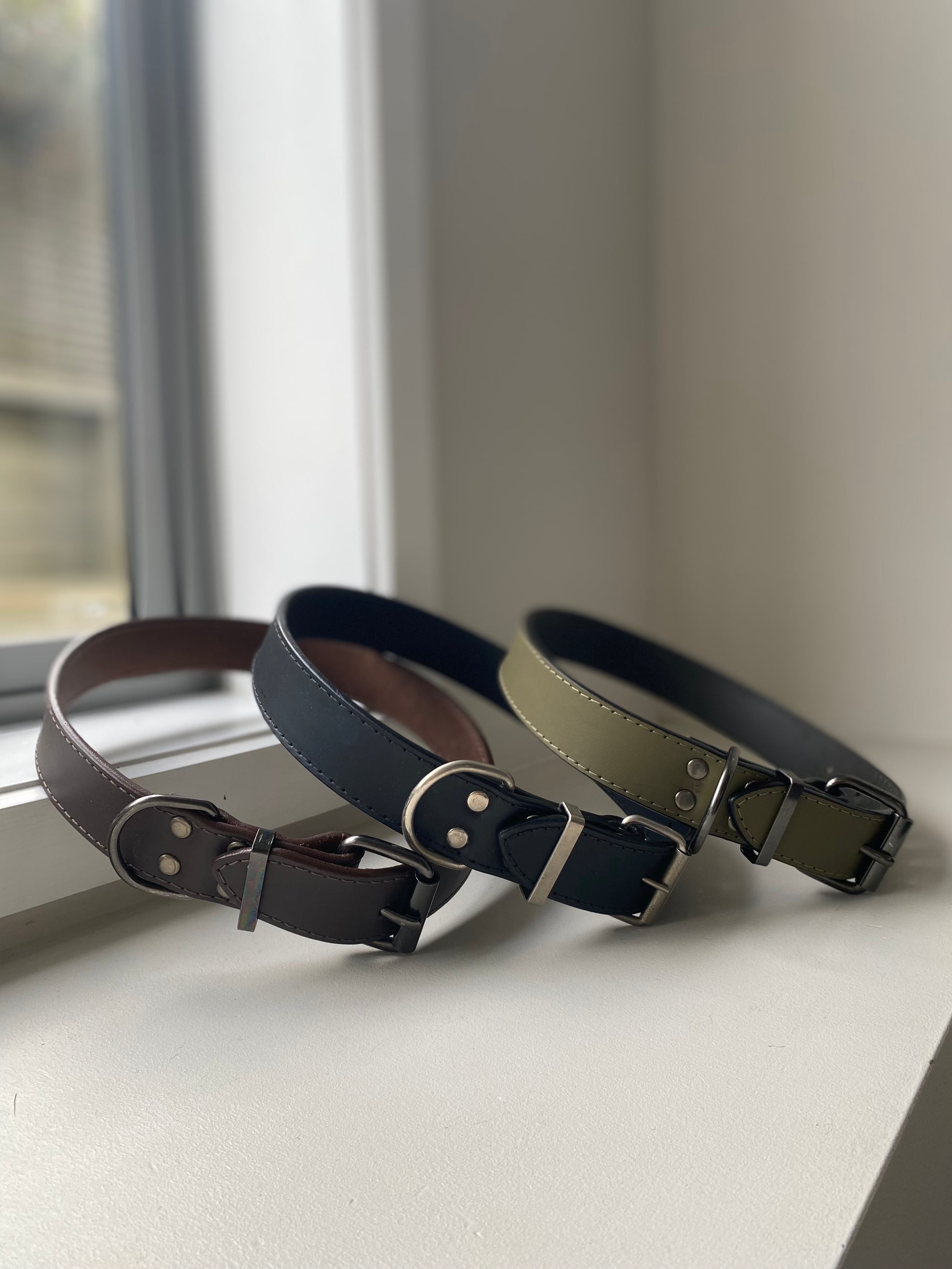 Three leather dog collars in different colors on a windowsill.