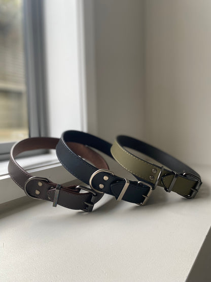 Three leather dog collars in different colors on a windowsill.
