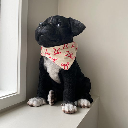 Black dog wearing a beige bandana with red bows on it