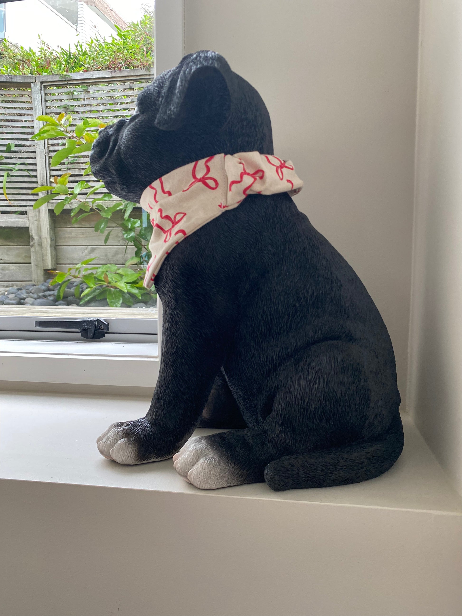 Black dog wearing a beige bandana with red bows on it