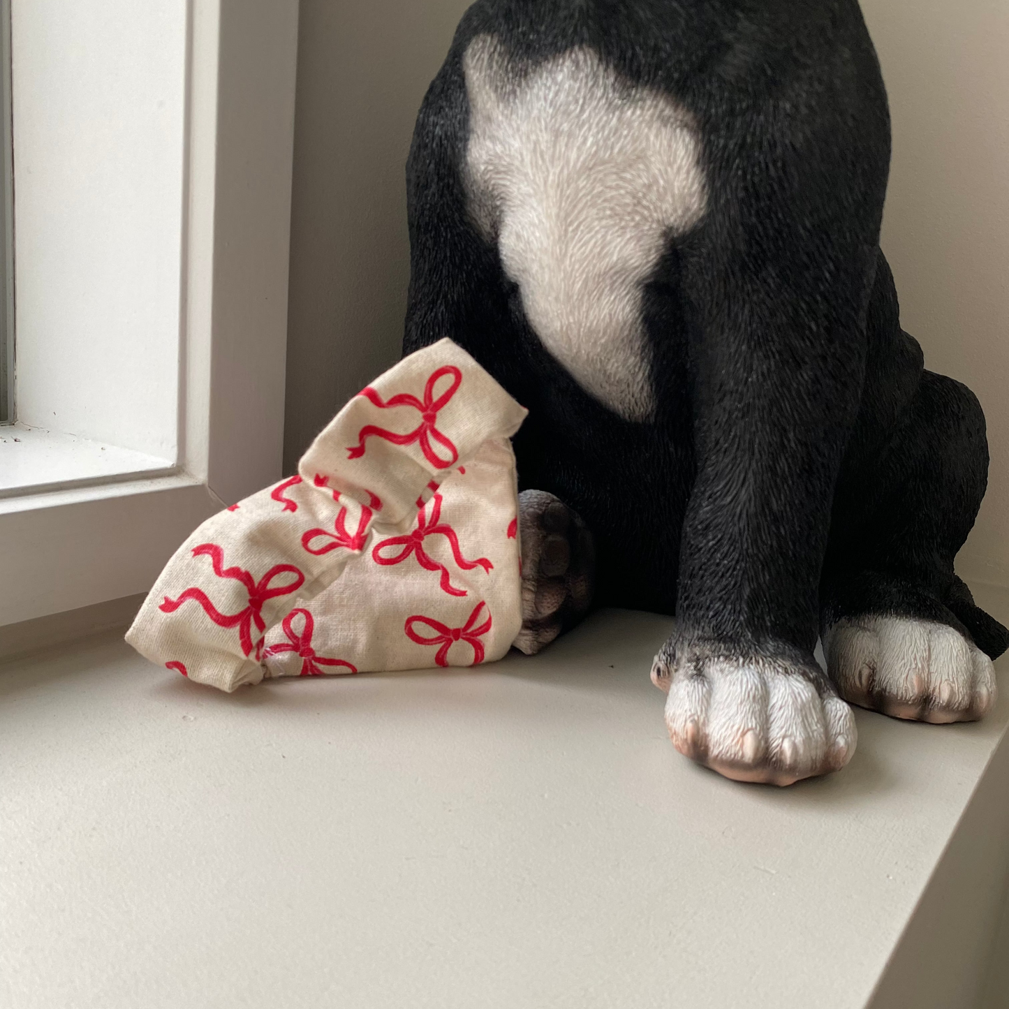 Black dog wearing a beige bandana with red bows on it