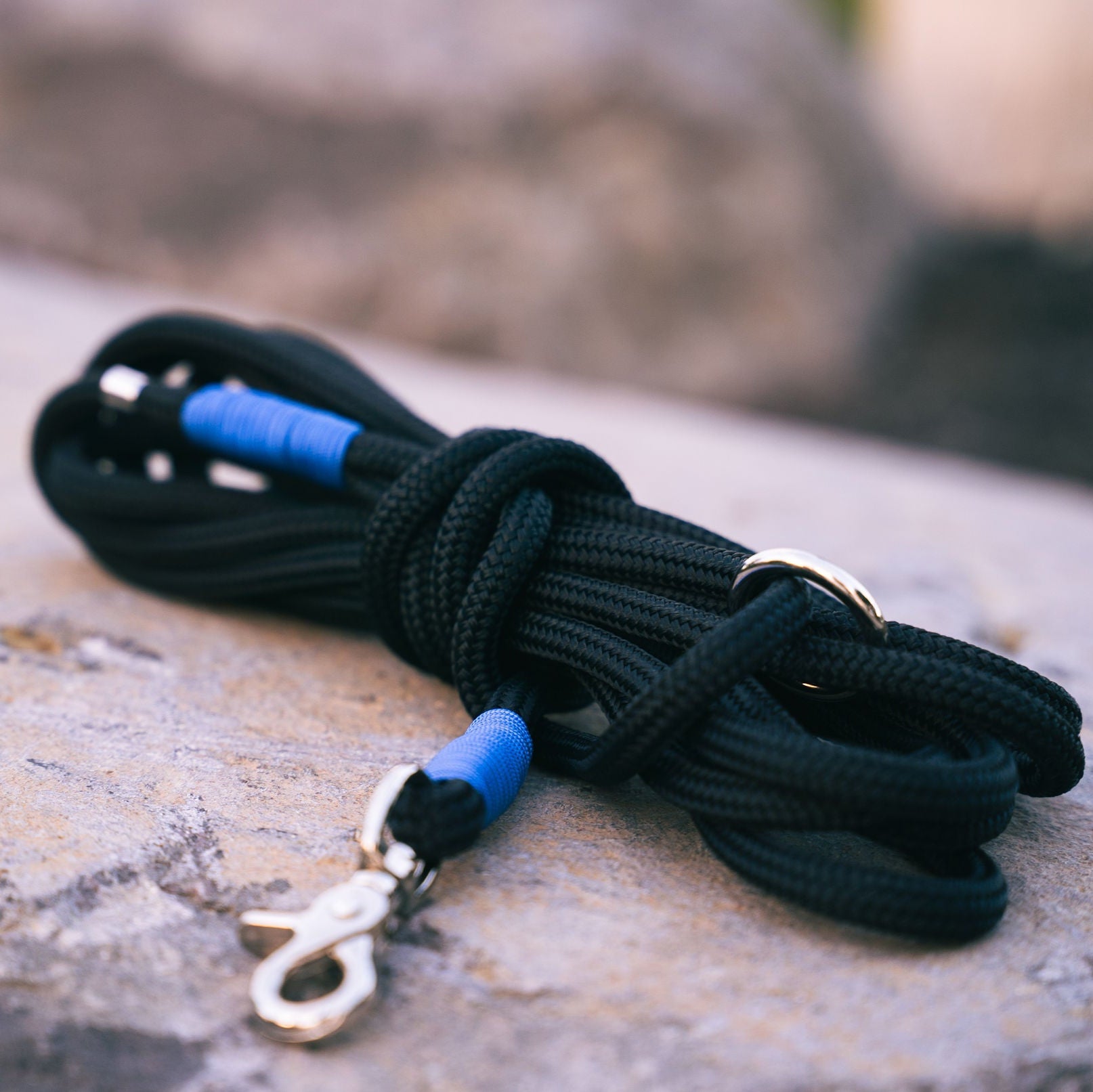 Black marine rope dog leash with blue accents and metal clasp on a stone surface