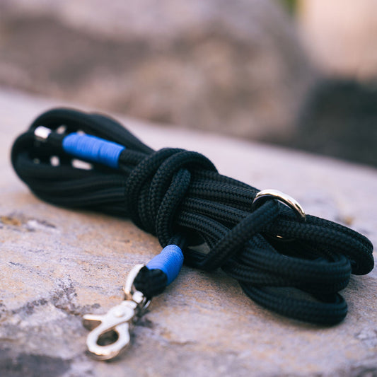 Black marine rope dog leash with blue accents and metal clasp on a stone surface