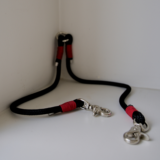 Dual dog leash attachment. This is made from black rope and it has got red paracord wrapped around the joins as an accent colour. 